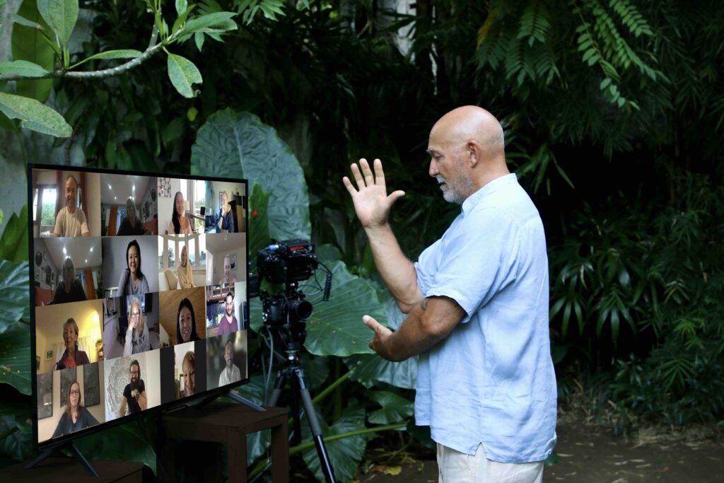 Qigong teacher leading a live online session outdoors with students joining via video call.
