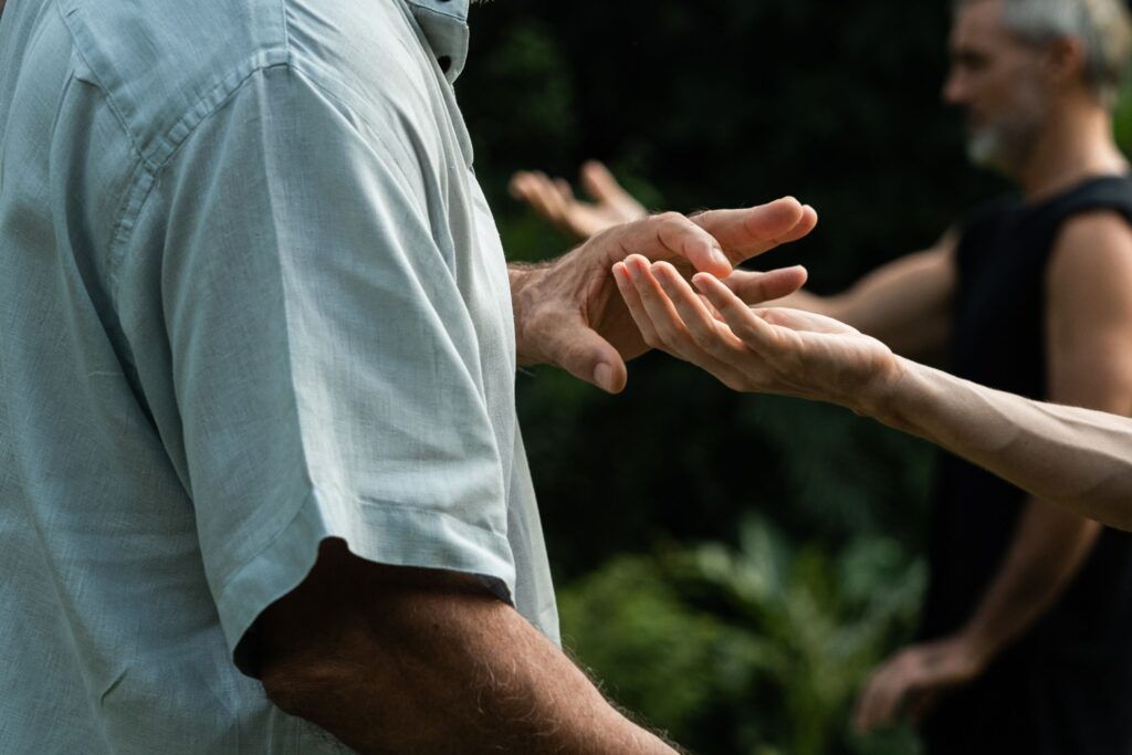 Two students practicing Qigong hand positioning outdoors, focusing on relaxed palms and energy awareness.