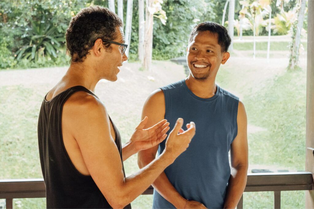 Two men discussing Qigong practice during an outdoor training session, smiling and engaging in conversation.